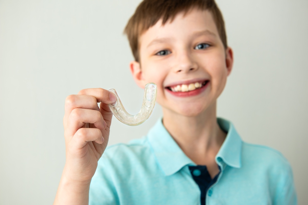 Child boy hold in hand invisible transparent aligners, invisalign bracer smile isolated on light gray background. Lifestyle concept Do Clear Aligners Cause Dry Mouth